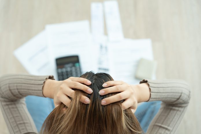 Stressed and headache woman with large bills or invoices no mone